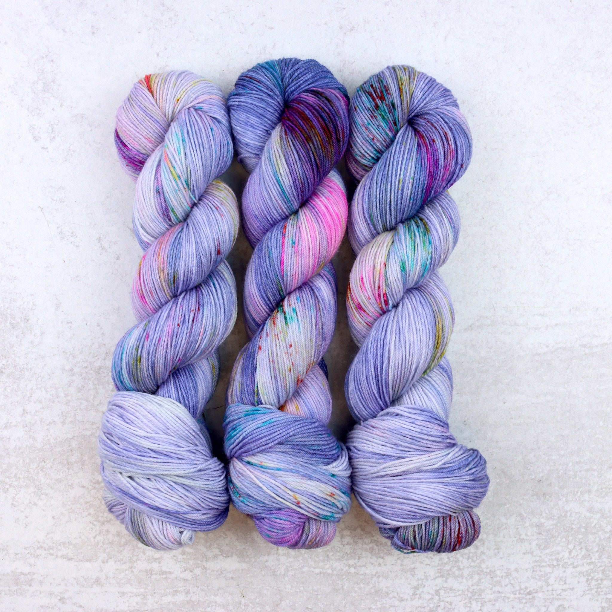 Hand dyed spekled yarn in purple with speckles of aqua, pink, orange and yellow.