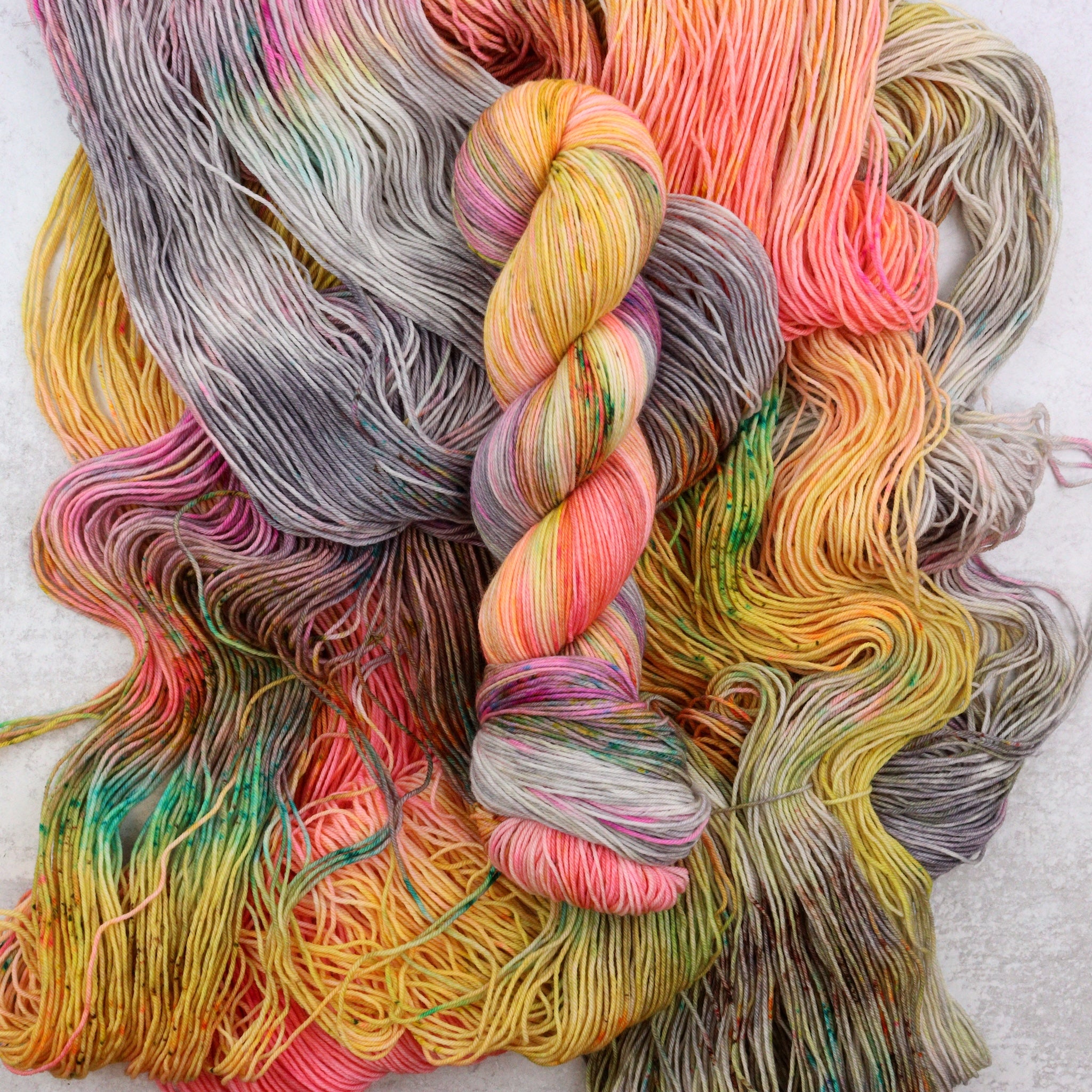 Variegated hand dyed yarn by Spun Right Round. Features Peach, pink, yellow, grey aqua and brown.