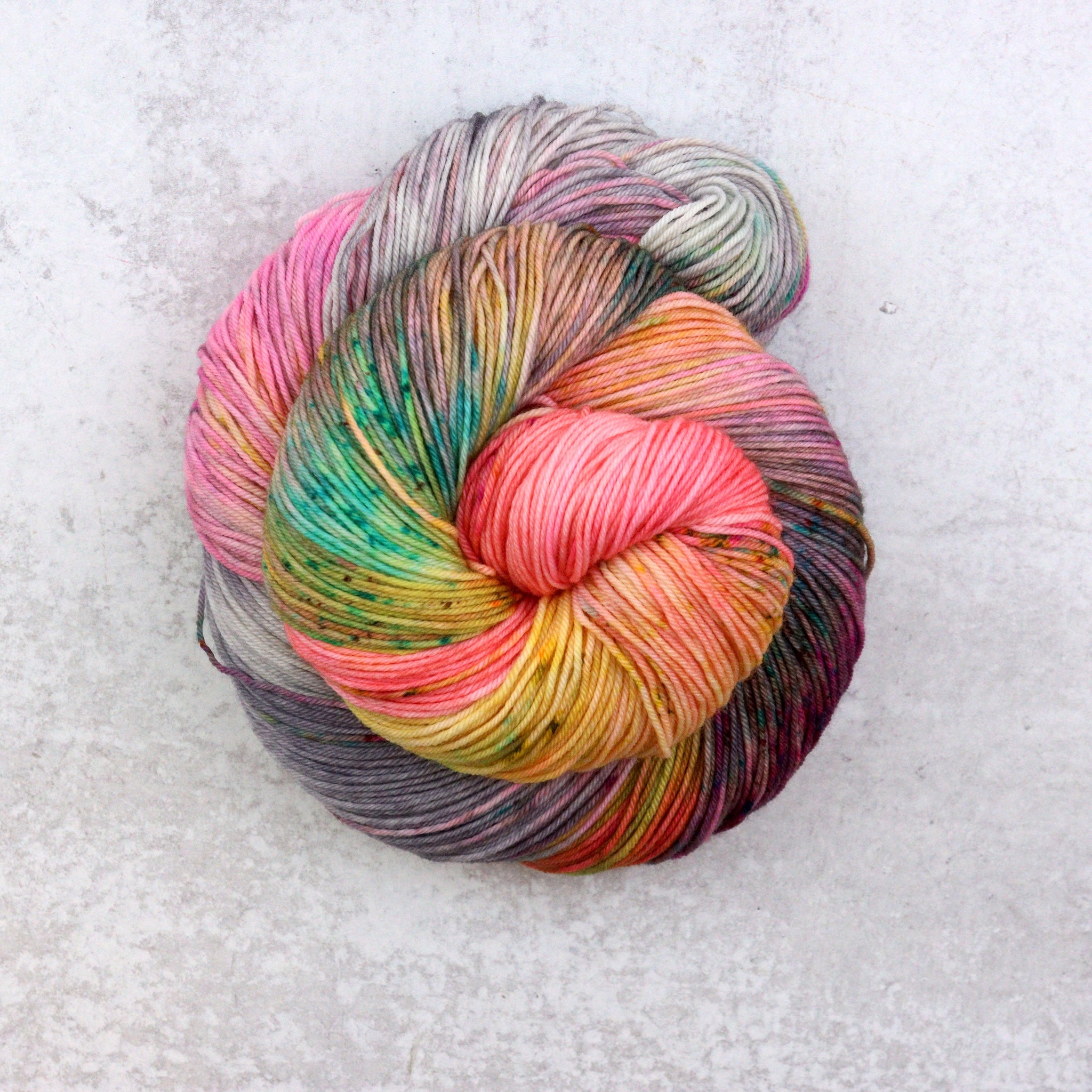 Variegated hand dyed sock yarn by Spun Right Round. Features Peach, pink, yellow, grey aqua and brown.