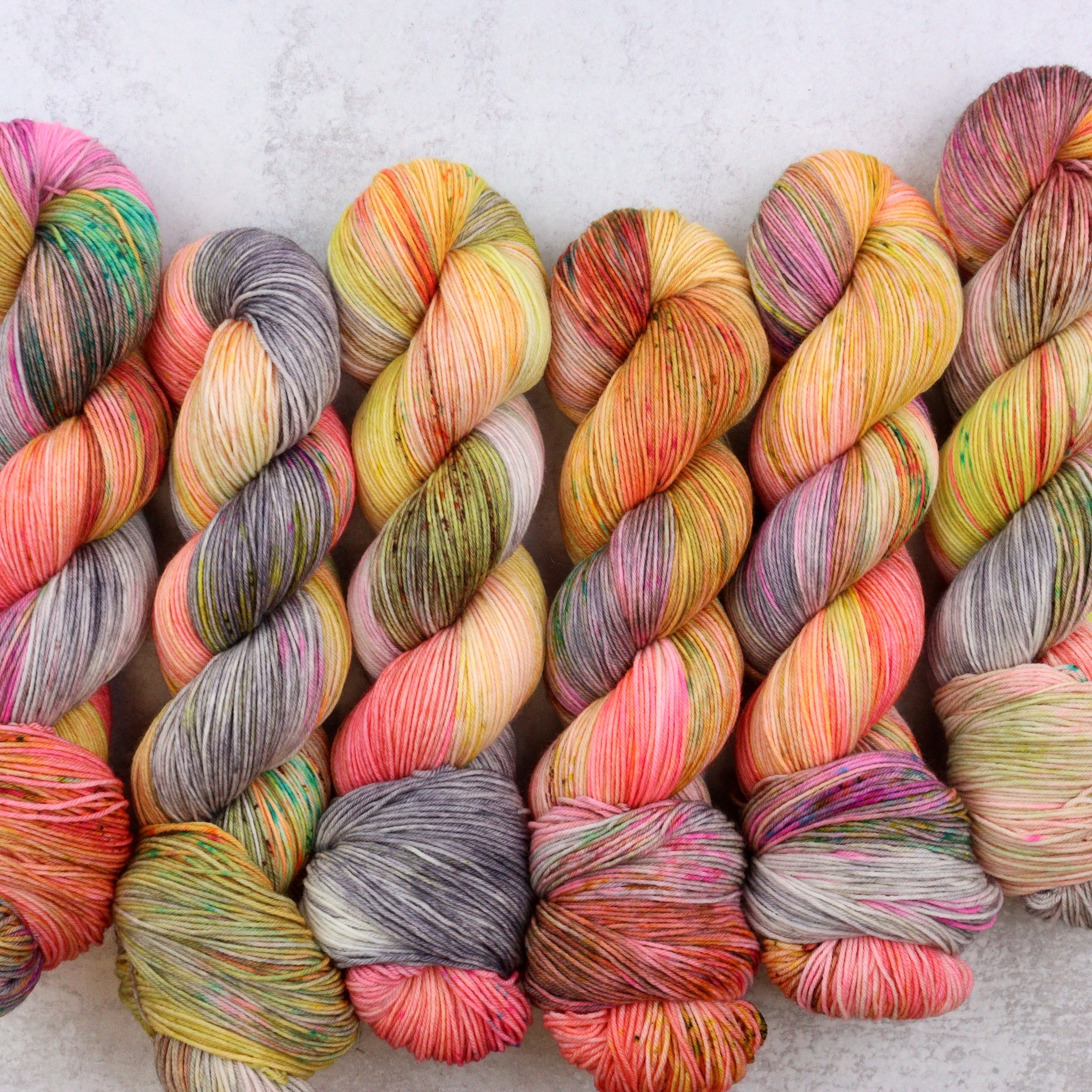 Variegated hand dyed yarn by Spun Right Round. Features Peach, pink, yellow, grey aqua and brown.