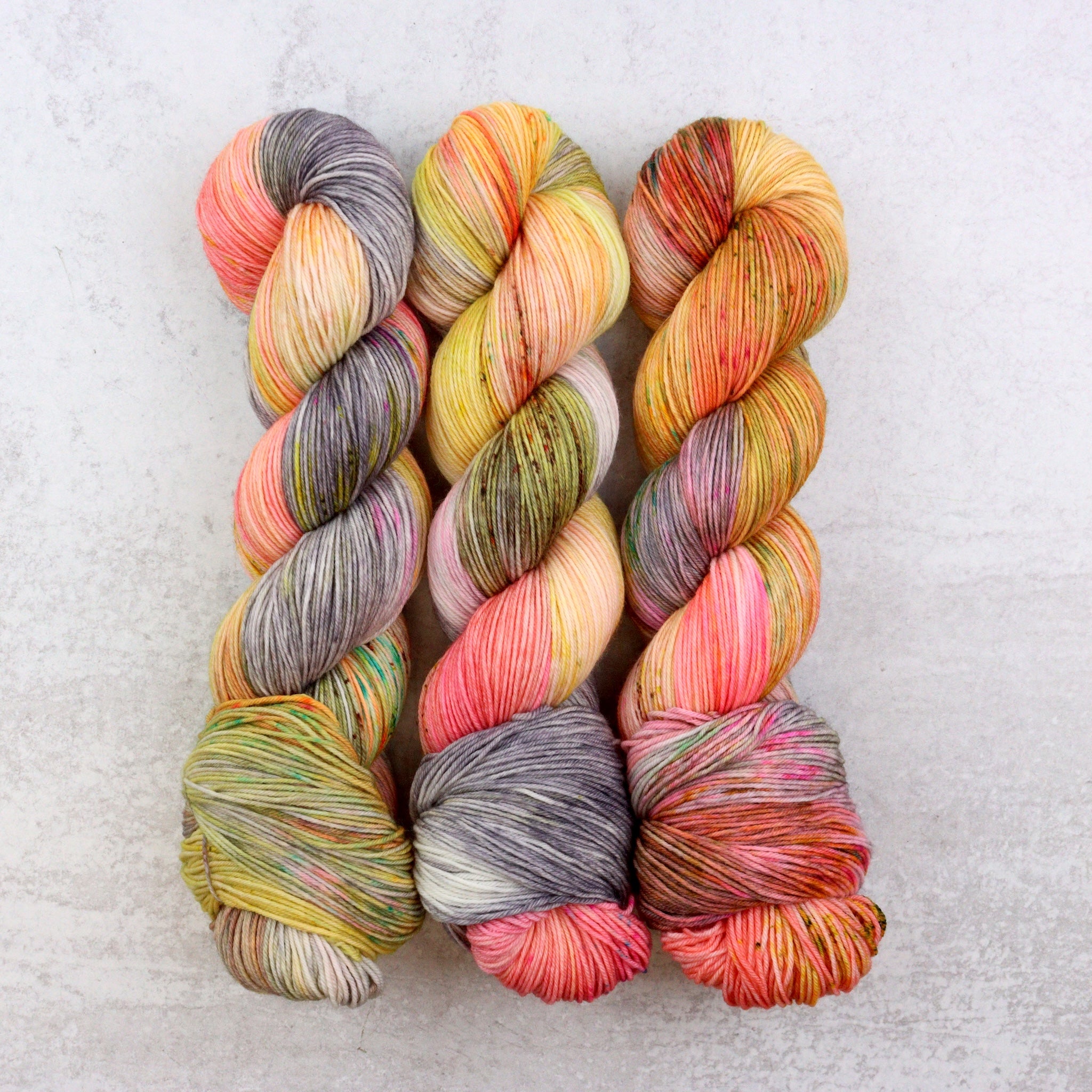 Variegated hand dyed yarn by Spun Right Round. Features Peach, pink, yellow, grey aqua and brown.