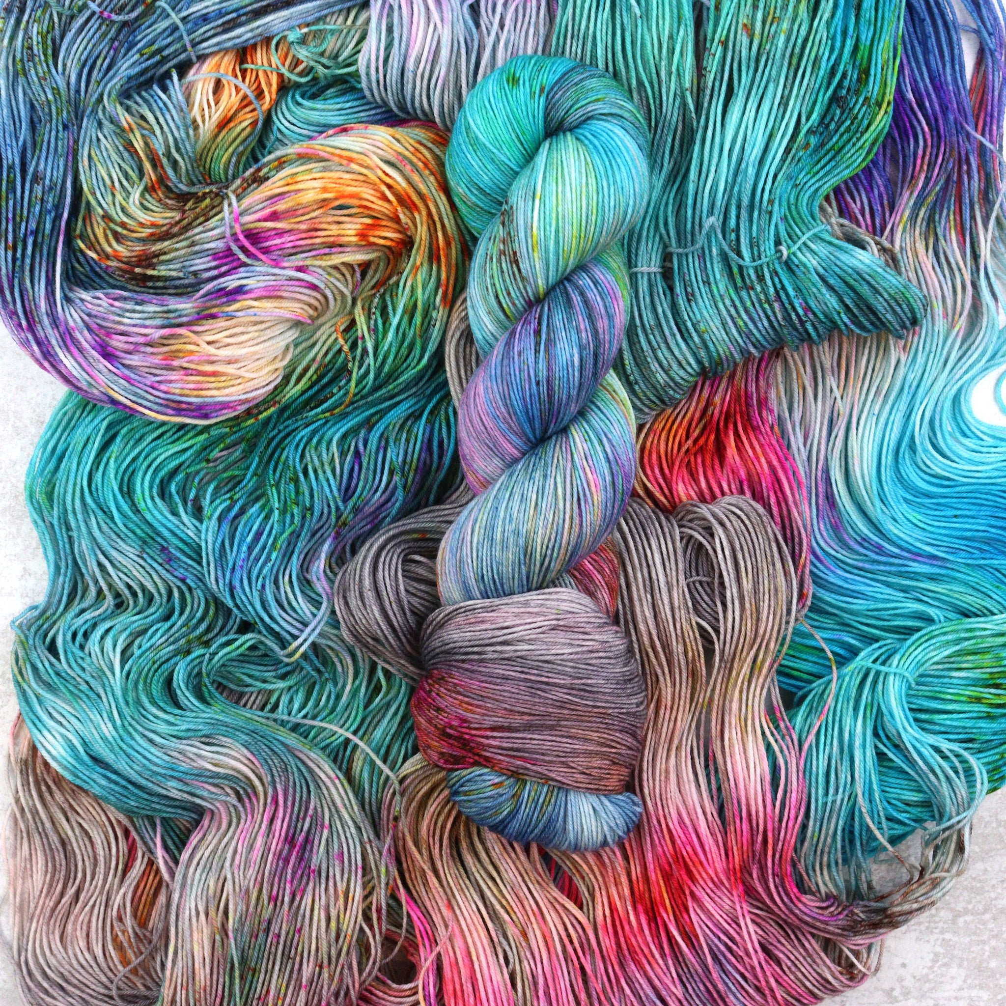 Variegated hand dyed sock yarn by Spun Right Round. Features pink, aqua, orange, green and brown speckles on a soft grey base.