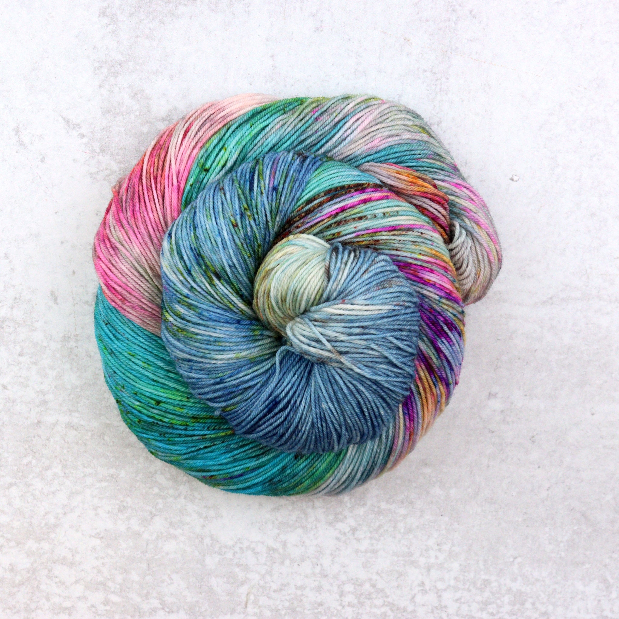 Variegated hand dyed sock yarn by Spun Right Round. Features pink, aqua, orange, green and brown speckles on a soft grey base.