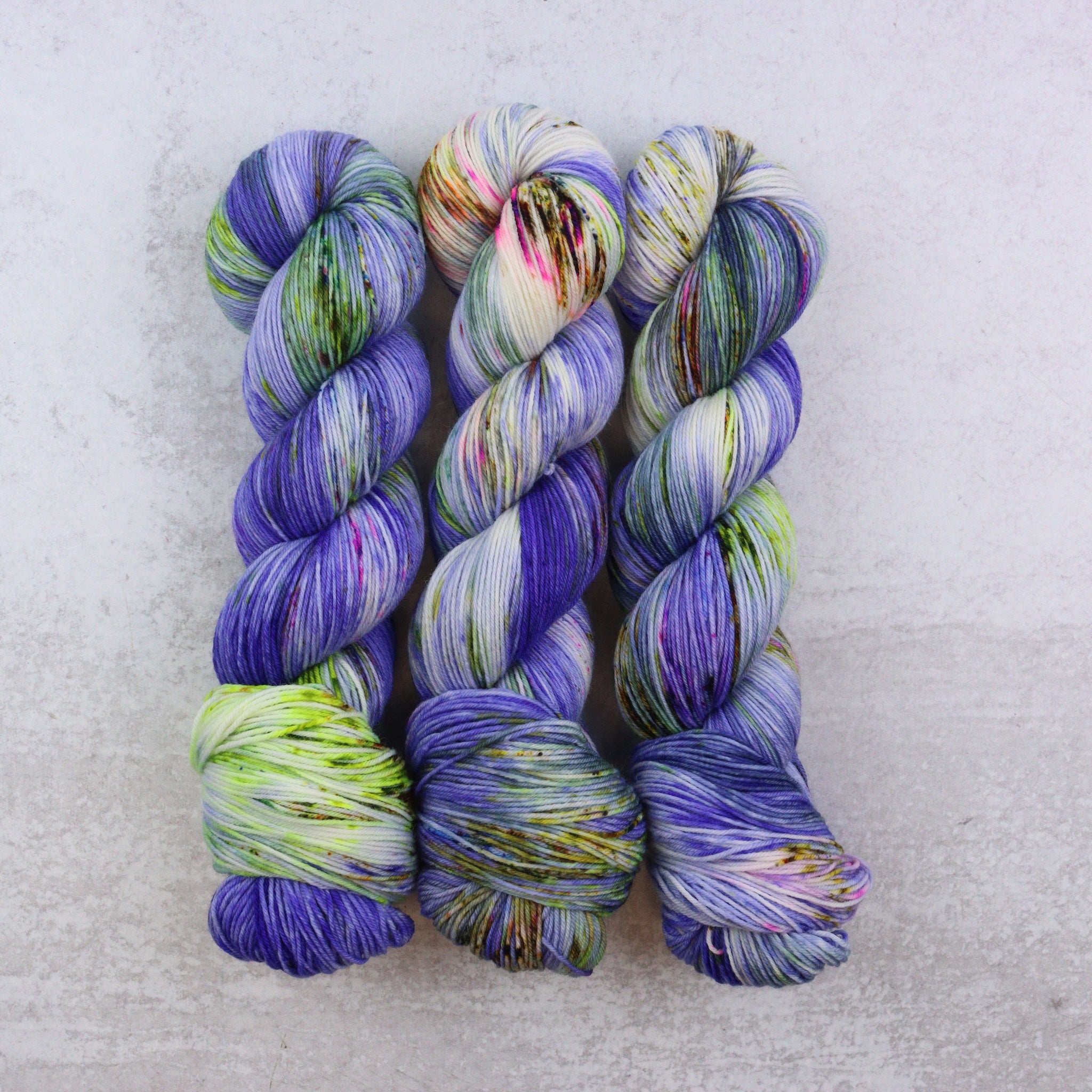 Three skeins of multicolored yarn on a light gray background