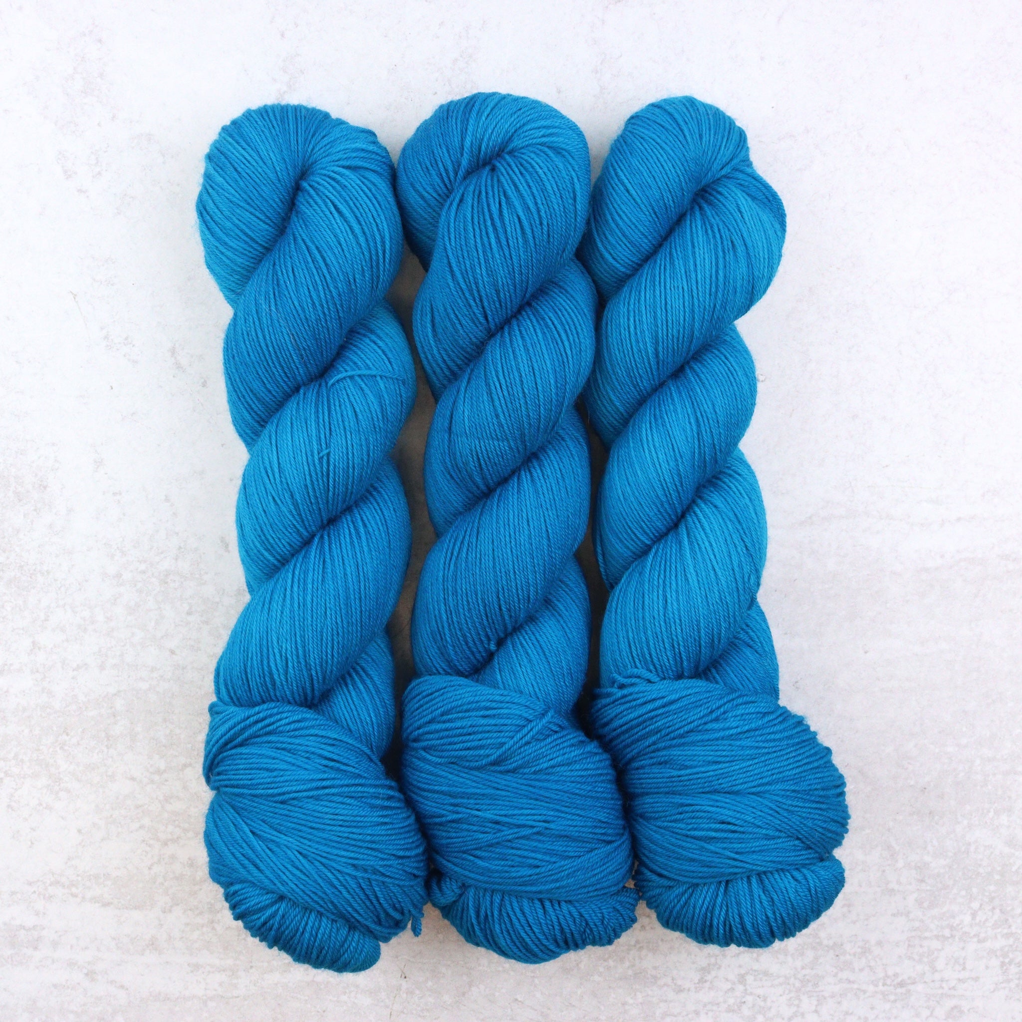 Hand dyed semi solid fingering weight yarn in a vibrant Caribbean blue.