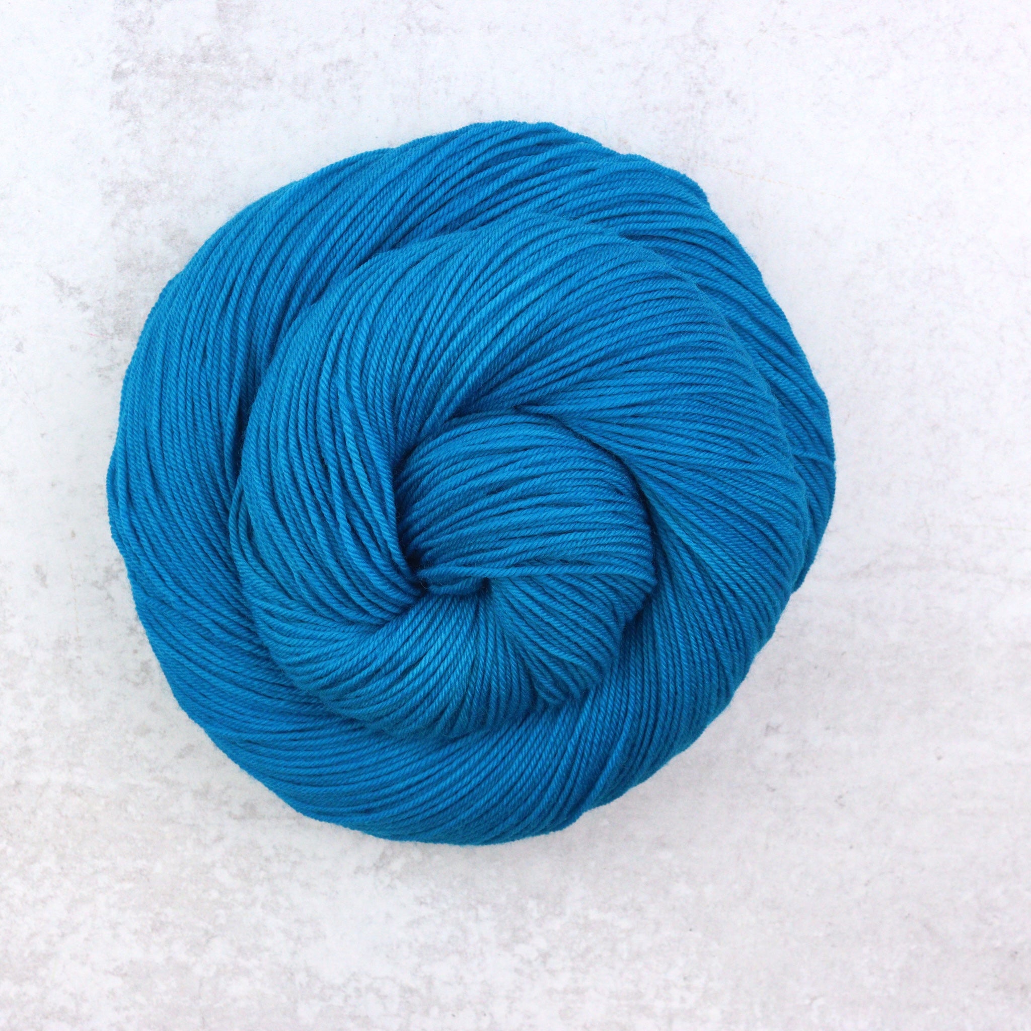 Hand dyed semi solid fingering weight yarn in a vibrant Caribbean blue.