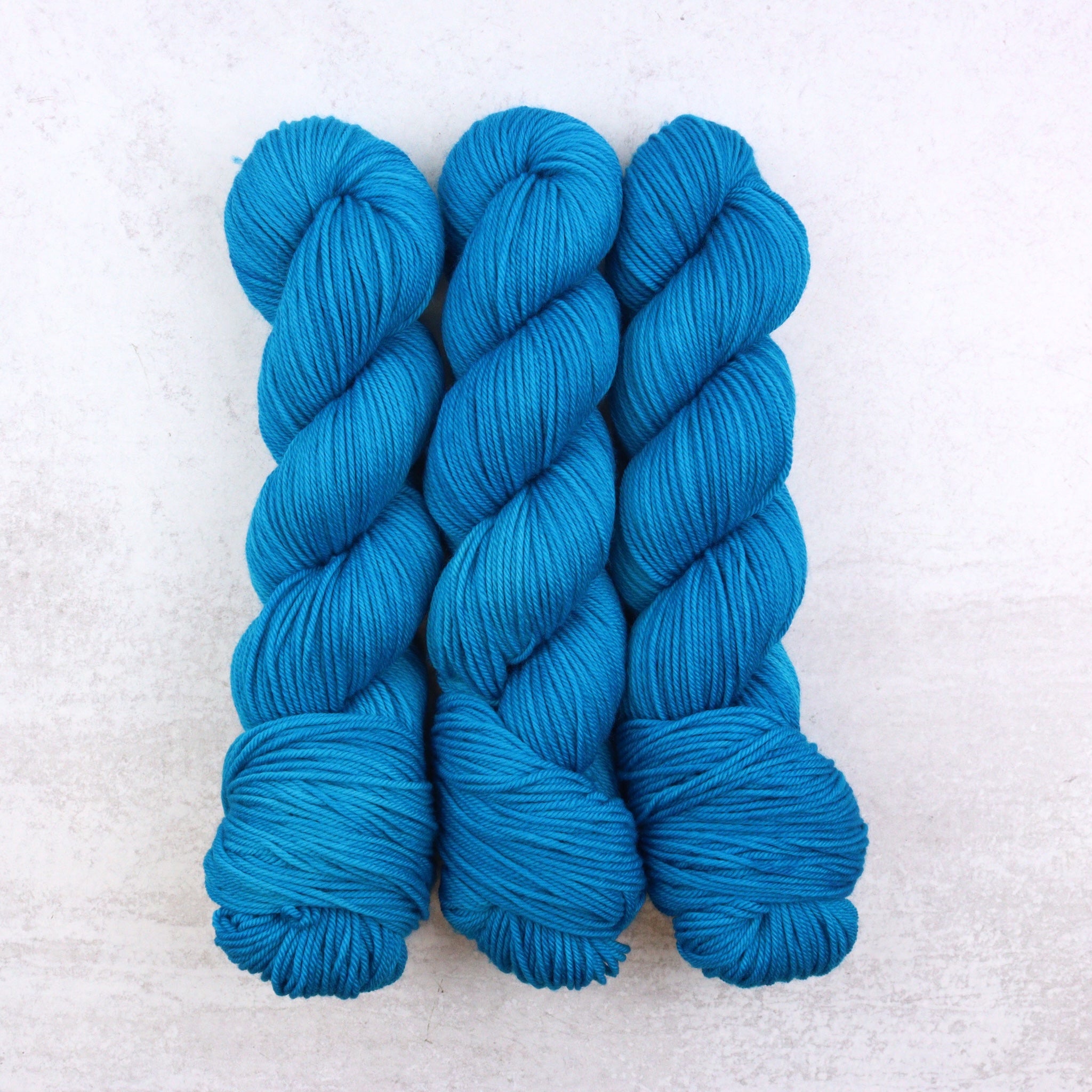 Hand dyed semi solid Dk weight yarn in a vibrant blue.
