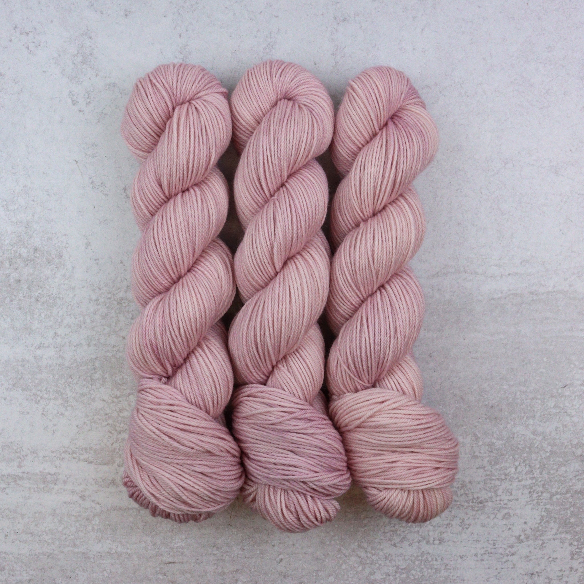 Three skeins of pink yarn on a light gray background