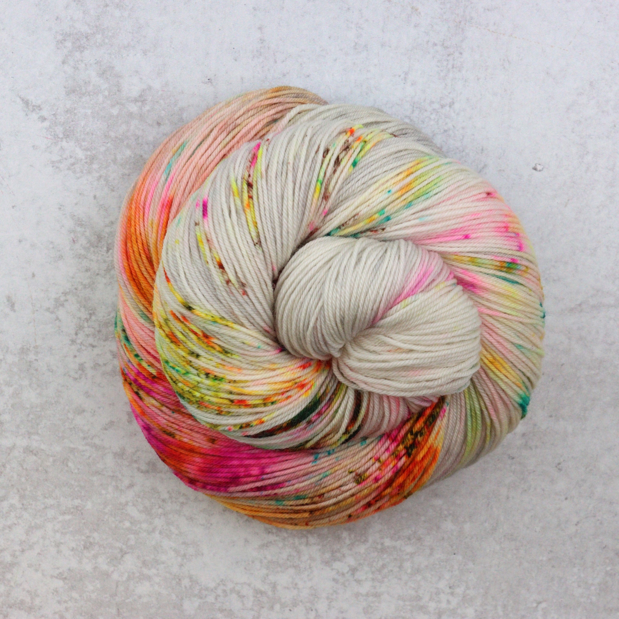 Hand dyed sock yarn by Spun Right Round. Features pink, aqua, green, orange and brown speckles on a soft grey base.