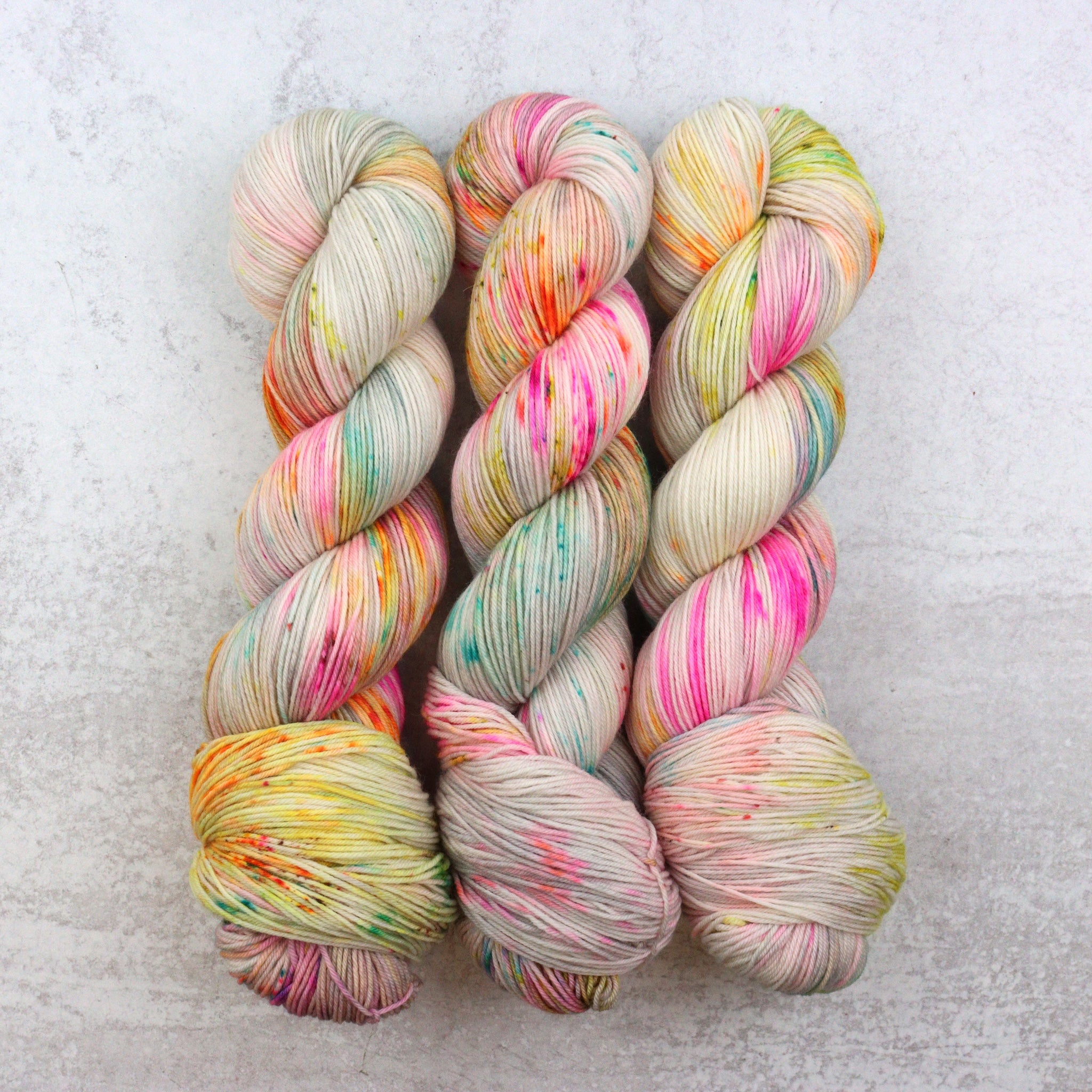 Hand dyed sock yarn by Spun Right Round. Features pink, aqua, green, orange and brown speckles on a soft grey base.