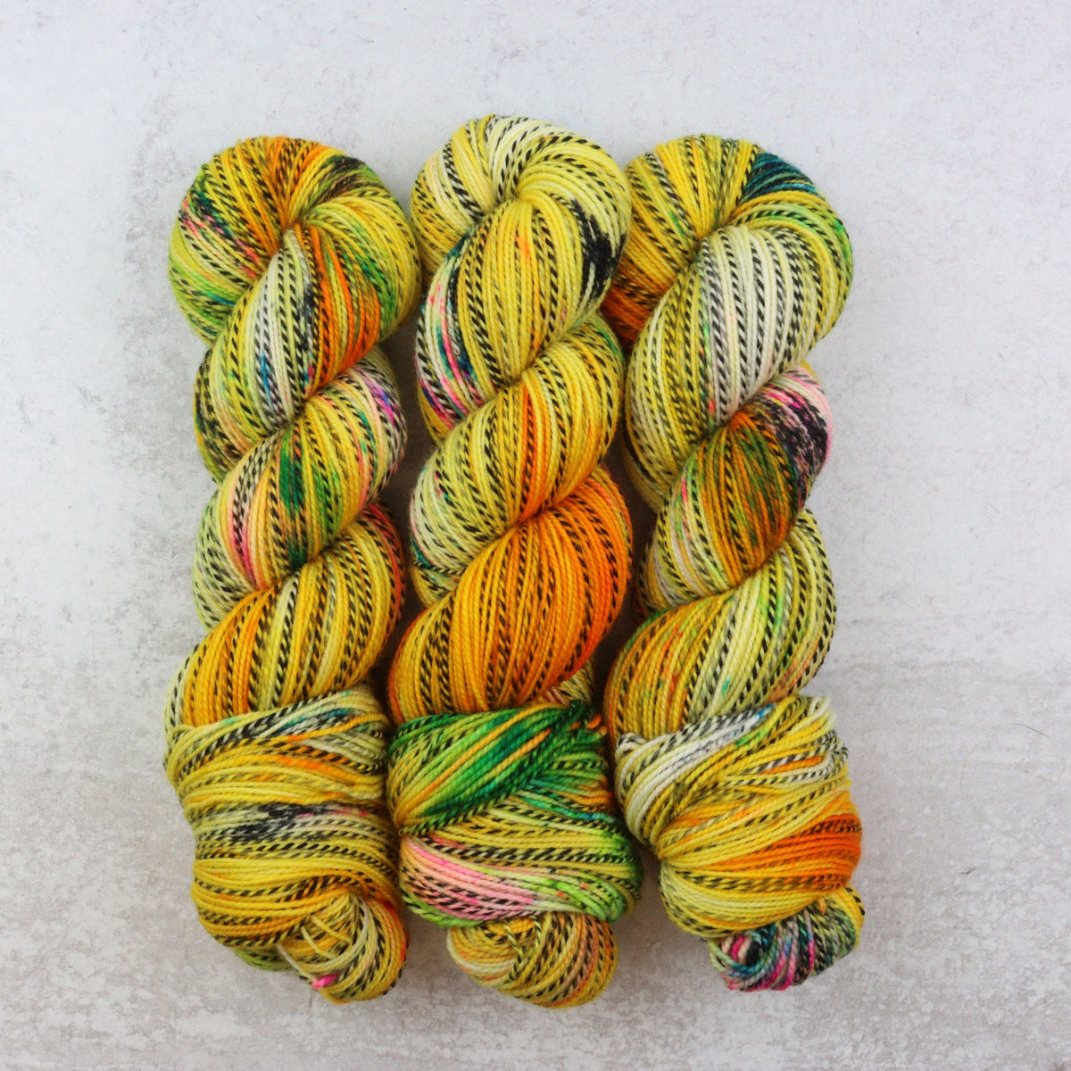 Bright yellow hand dyed yarn with pink, black, green, aqua and orange speckles.