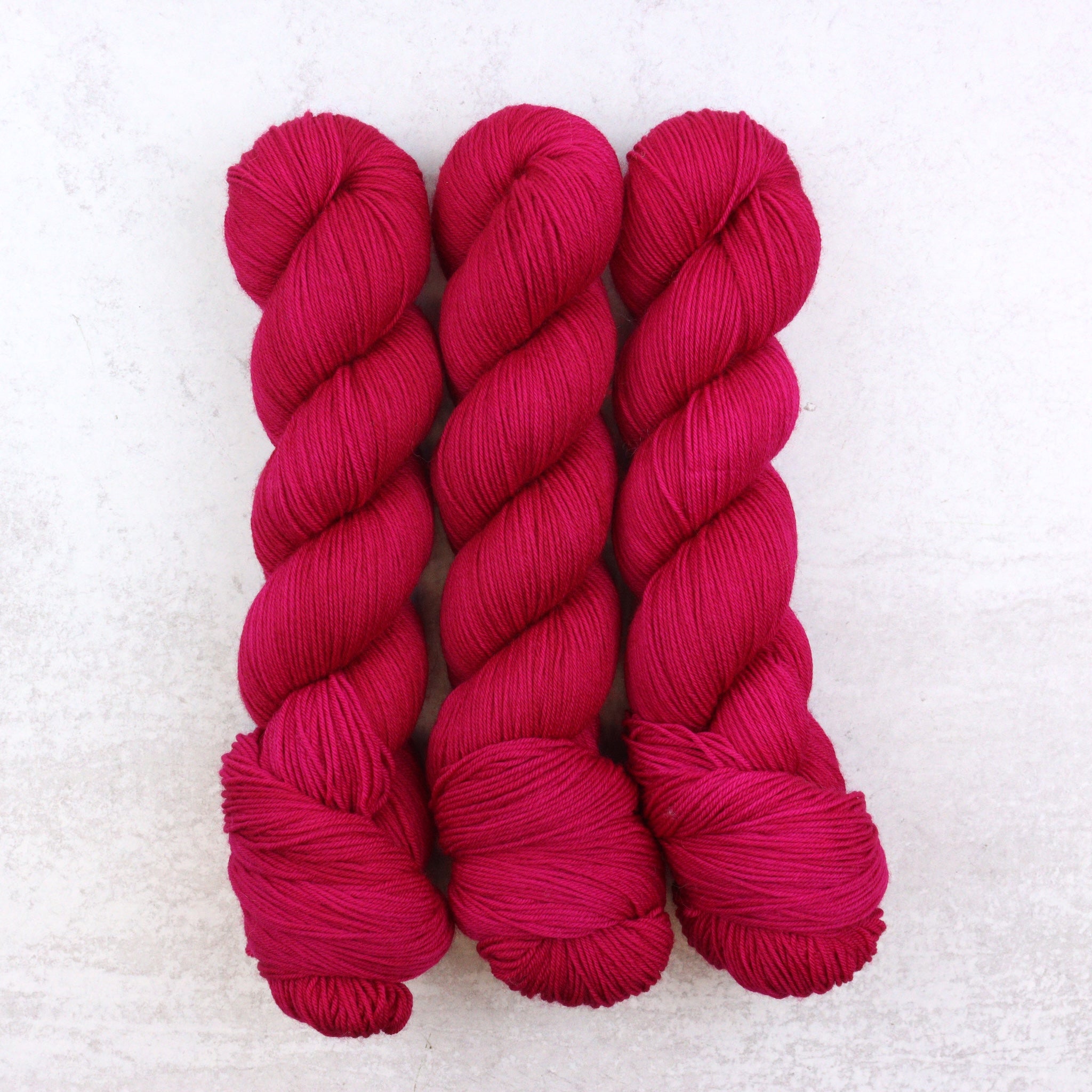 Hand dyed semi solid fingering weight yarn in a vibrant Magenta Pink that leans red.