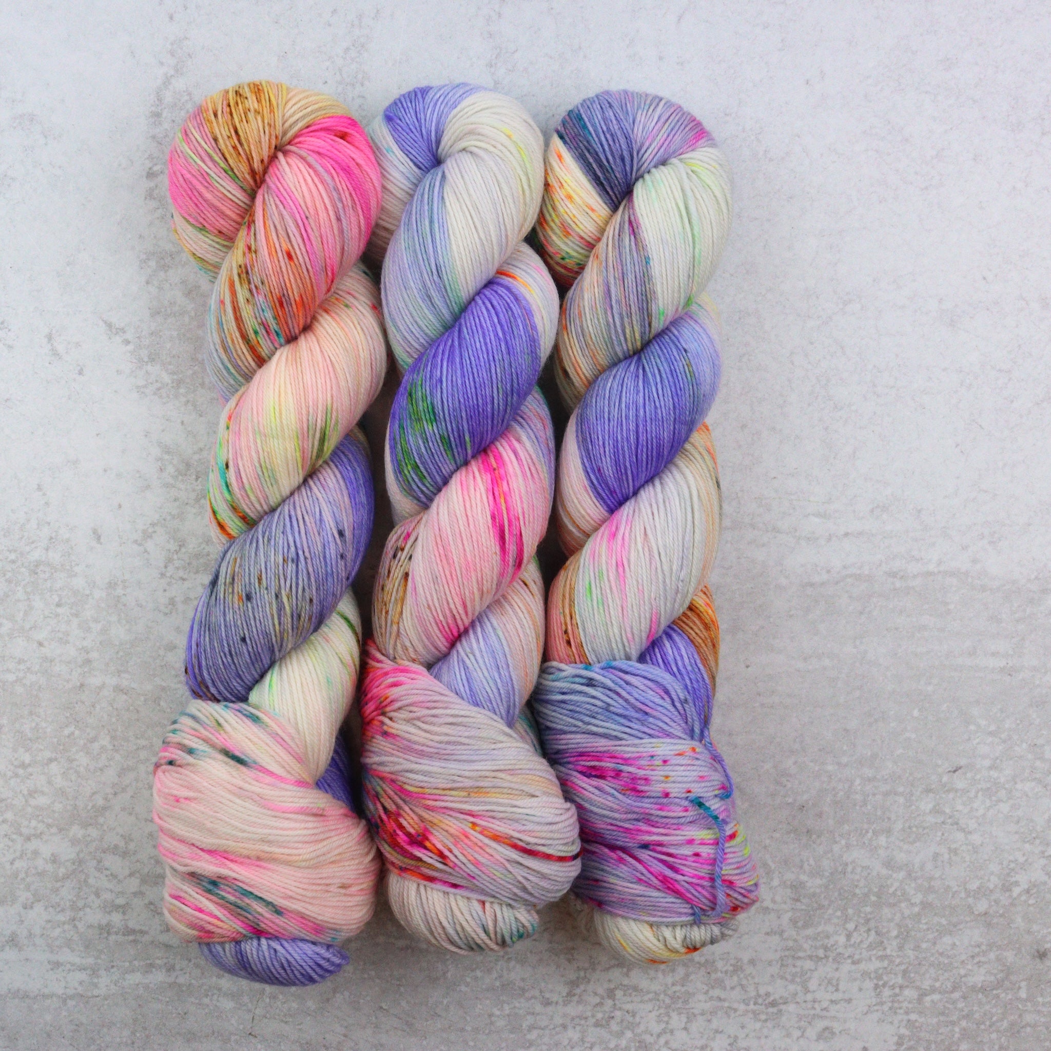 A hand dyed speckled yarn with purple, orange, green, pink, brown and aqua.