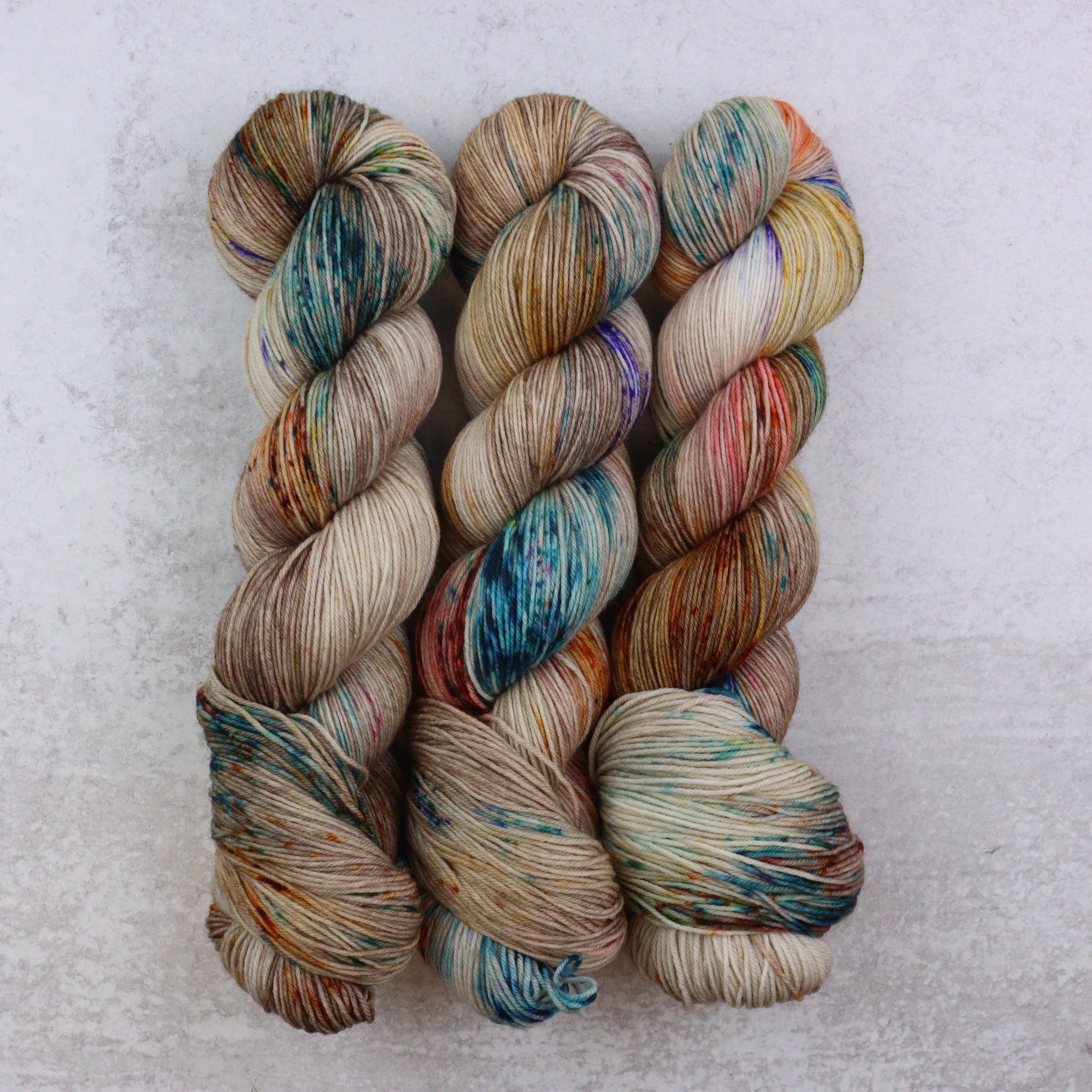 Three skeins of multicolored yarn on a light gray background
