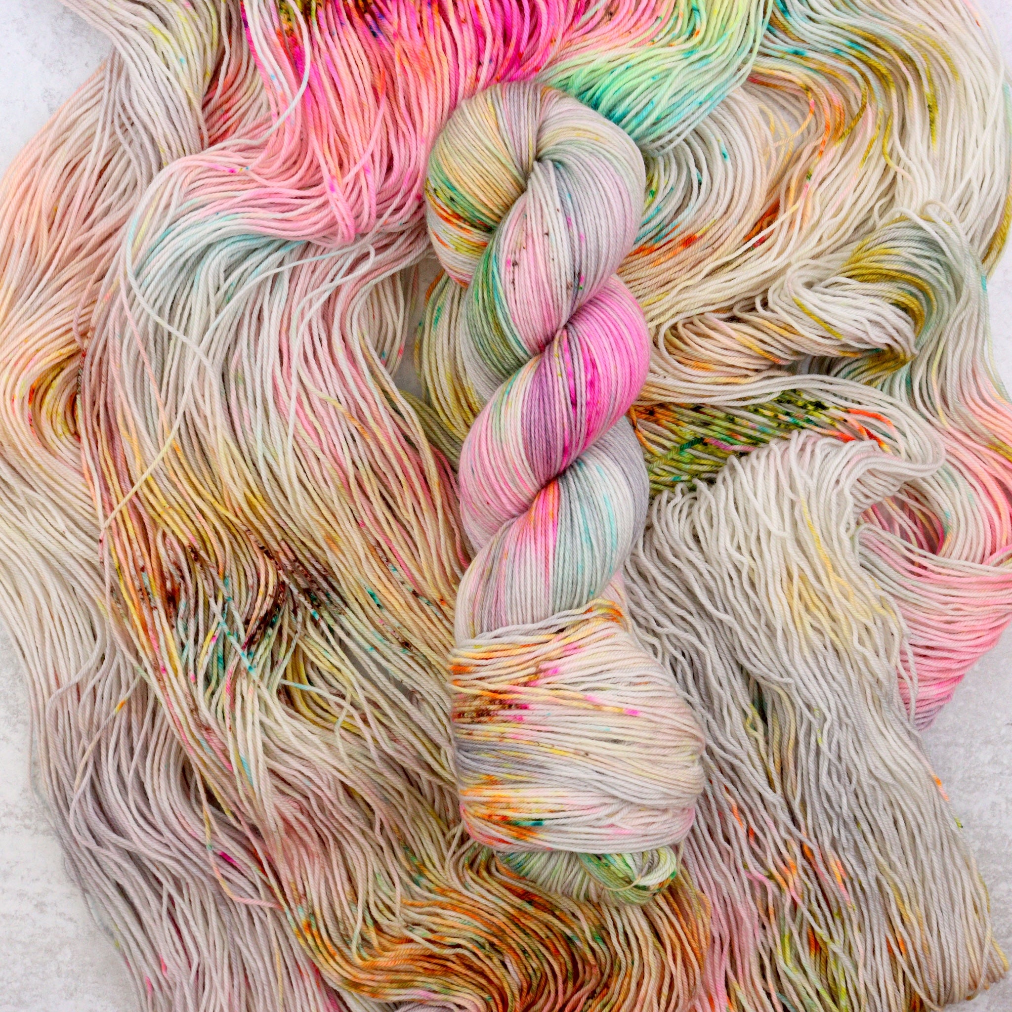 Variegated hand dyed  sock yarn by Spun Right Round. Features pink, aqua, orange, green and brown speckles on a soft grey base.