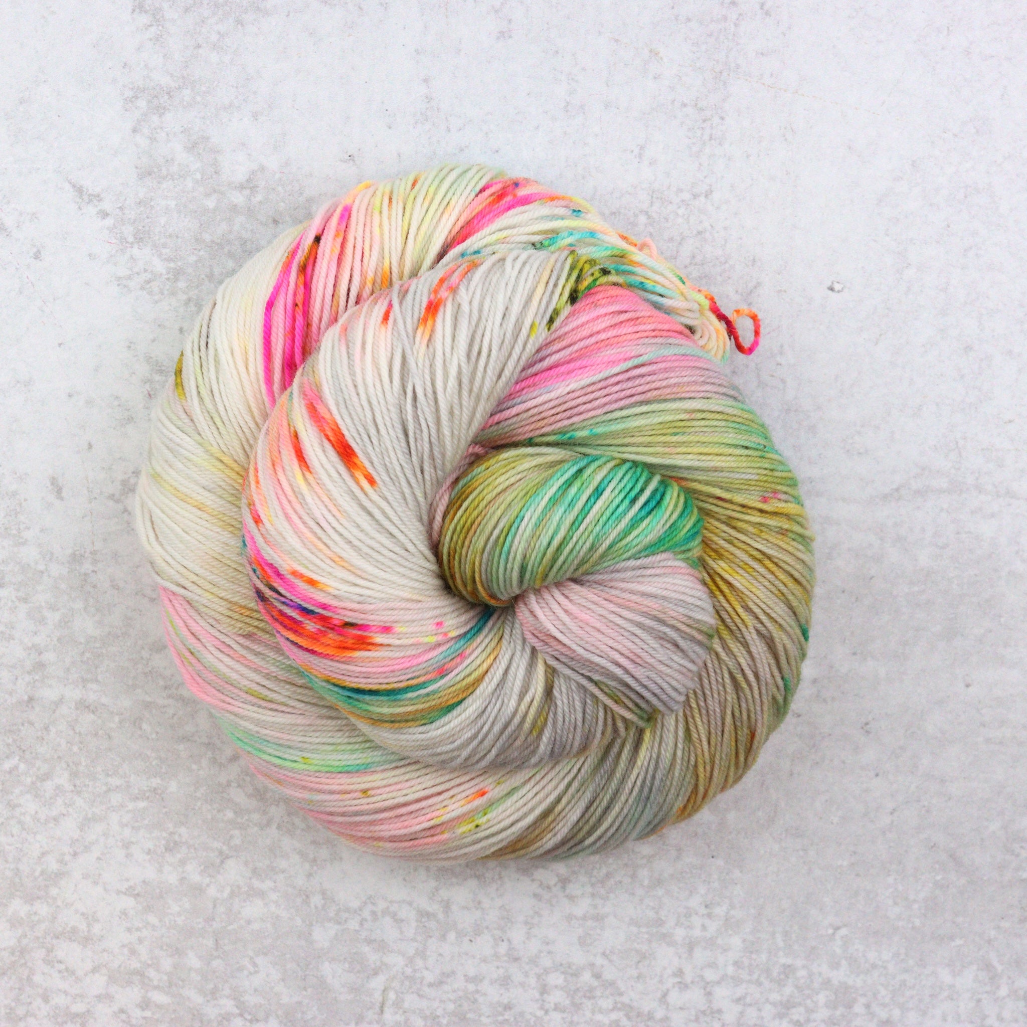 Variegated hand dyed  sock yarn by Spun Right Round. Features pink, aqua, orange, green and brown speckles on a soft grey base.