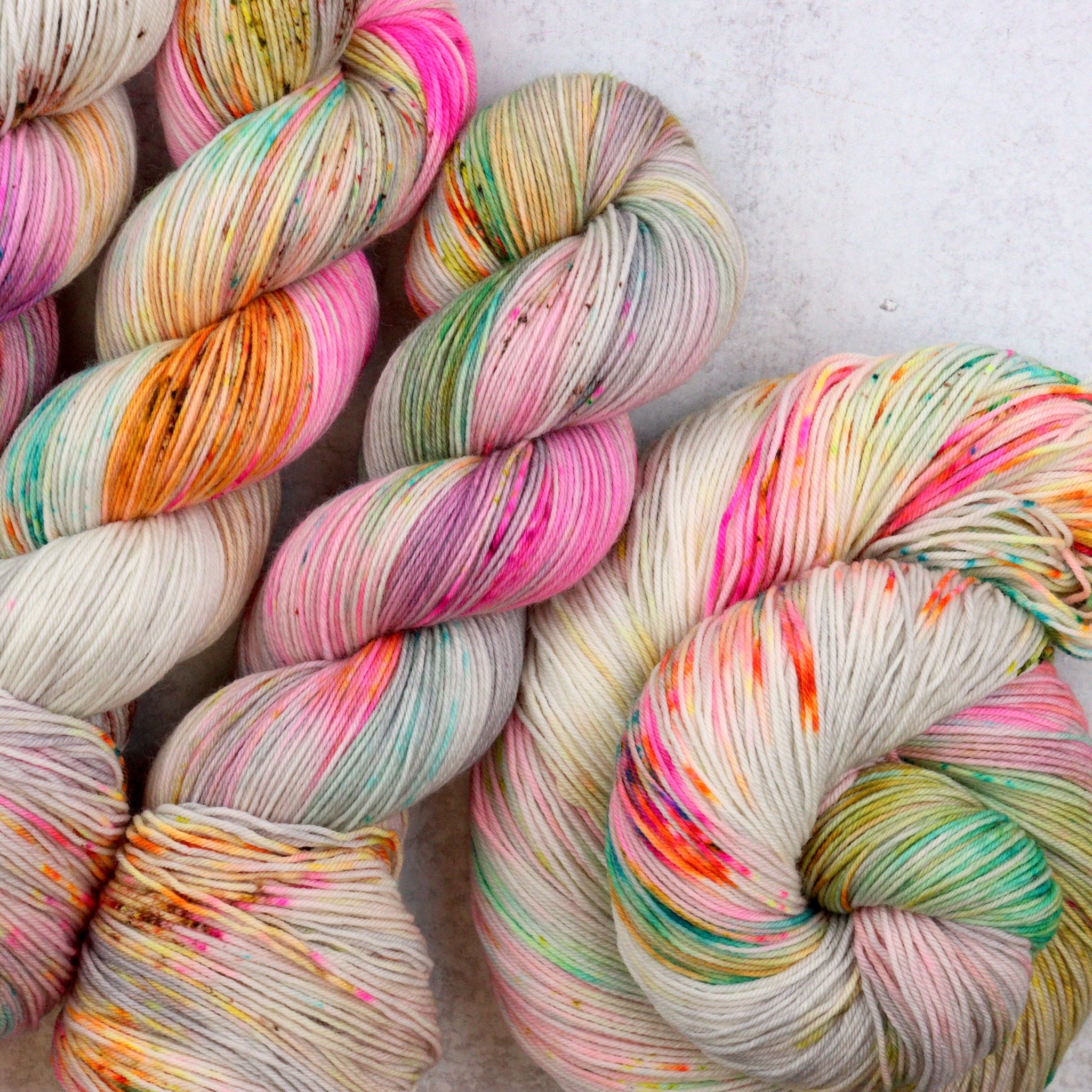 Variegated hand dyed  sock yarn by Spun Right Round. Features pink, aqua, orange, green and brown speckles on a soft grey base.