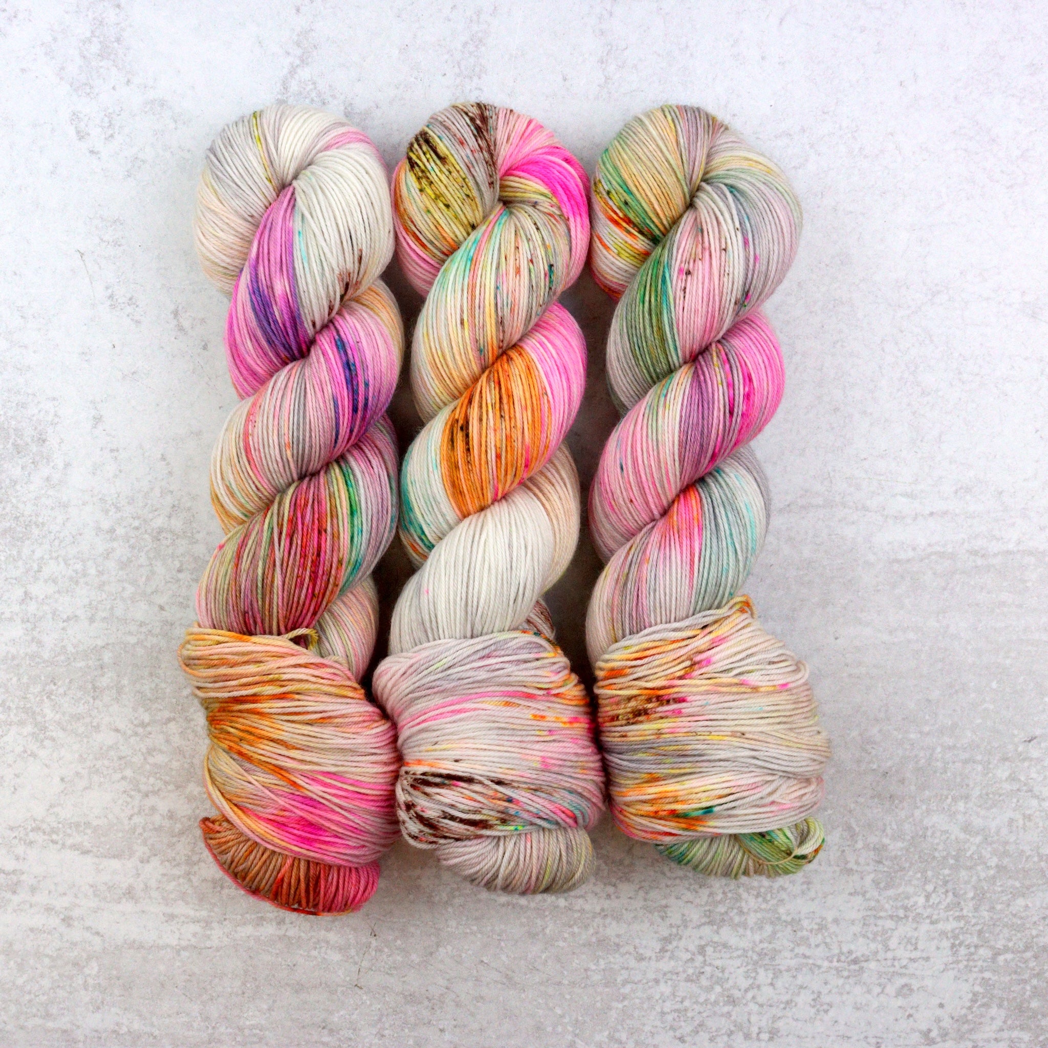 Variegated hand dyed  sock yarn by Spun Right Round. Features pink, aqua, orange, green and brown speckles on a soft grey base.